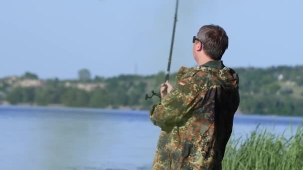 Amante de la pesca sostiene una caña en su mano y gira el carrete lanza una caña de pescar — Vídeo de stock
