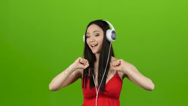 Chica escucha música alegre a través de auriculares y bailes. Pantalla verde — Vídeos de Stock