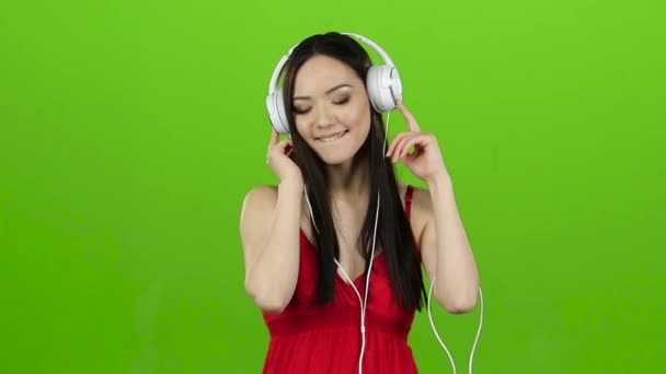 女の子は、ヘッドフォンを通して明るく、エネルギッシュな音楽を聴きます。緑色の画面。スローモーション — ストック動画
