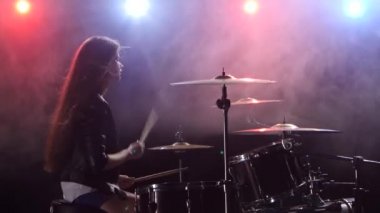 Kız gülümser ve davul çalıyor. Siyah duman arka plan. Arkadan kırmızı mavi ışık. Yan görünüm