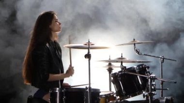 Davulcu bir deri ceketli enerjik müzik çalar. Siyah duman arka plan. Yan görünüm