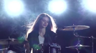 Davulcu bir rock konserinde bateri çalıyor. Siyah duman arka plan. Arkadan ışık. Ağır çekim