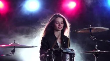 Kız gülümser ve davul çalıyor. Siyah duman arka plan. Arkadan kırmızı mavi ışık. Ağır çekim