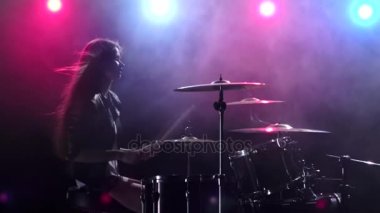 Kız gülümser ve davul çalıyor. Siyah duman arka plan. Arkadan kırmızı mavi ışık. Yan görünümü. Ağır çekim