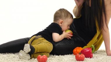 Küçük çocuk annesi yanında bir elma yiyor. Beyaz arka plan