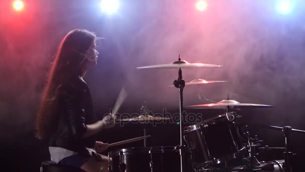 Meisje speelt drums en glimlacht. Zwarte rook achtergrond. Rood blauw licht van achteren. Zijaanzicht — Stockvideo