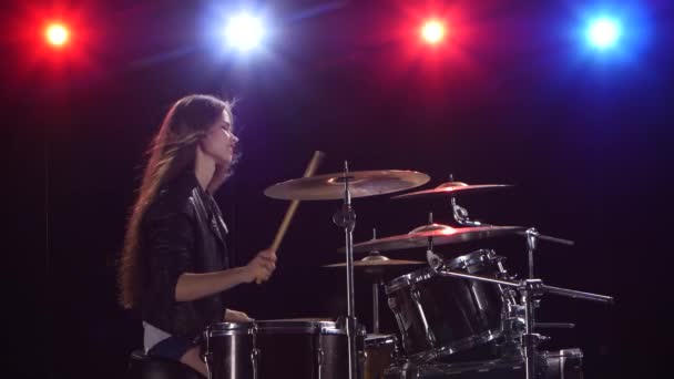 Девушка играет на барабанах. Чёрный фон. Красный синий свет сзади. Вид сбоку — стоковое видео