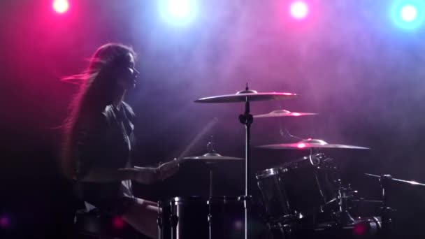 Meisje speelt drums en glimlacht. Zwarte rook achtergrond. Rood blauw licht van achteren. Zijaanzicht. Slow motion — Stockvideo