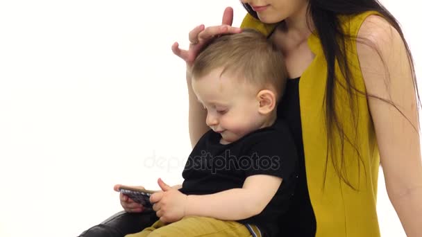 Жінка сидить на підлозі зі своєю дитиною, вона погладжує його волосся. Білий фон — стокове відео