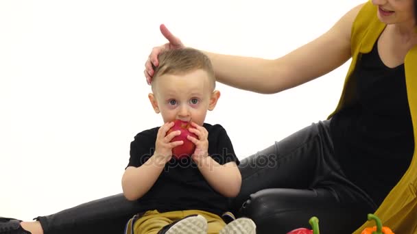 Criança pequena come uma maçã, ao lado de sua mãe. Fundo branco — Vídeo de Stock