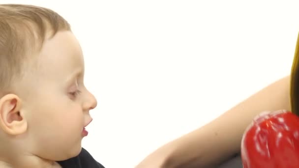 A mãe e o filho estão sentados no chão a segurar vegetais. Fundo branco. Fechar — Vídeo de Stock