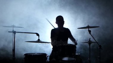 Müzisyen profesyonel olarak iyi müzik sopa kullanma davul çalıyor. Dumanlı arka plan. Siluet