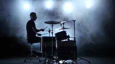 Müzisyen profesyonel olarak iyi müzik sopa kullanma davul çalıyor. Dumanlı arka plan. Siluet