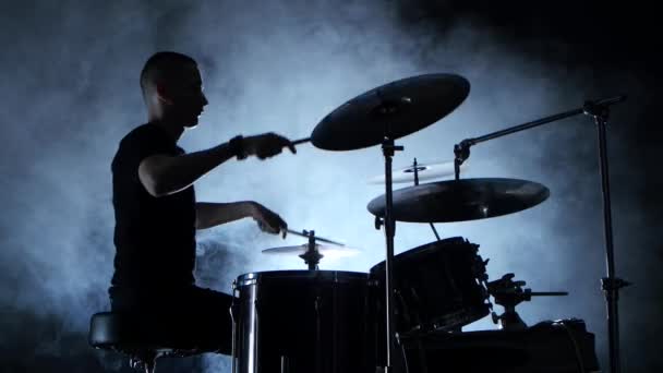 Energický hudebník hraje na bicí dobrou hudbu. Černé kouřové pozadí. Boční pohled. Silueta