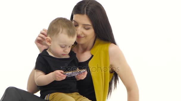 女性は彼女の赤ん坊を床に座って、彼女は彼の髪をなでます。白い背景。スローモーション — ストック動画