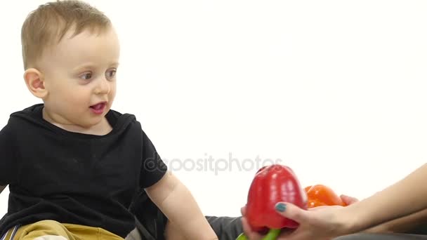 Mutter und Kind sitzen auf dem Boden, um viel Gemüse und Obst herum. weißer Hintergrund. Zeitlupe. Nahaufnahme — Stockvideo