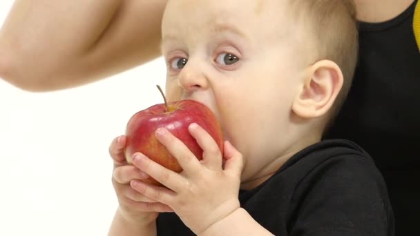 Ребенок ест яблоко рядом с матерью. Белый фон. Медленное движение. Закрыть — стоковое видео
