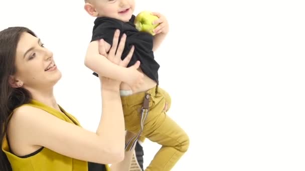 Mãe circula seu filho em seus braços, o bebê come uma maçã. Fundo branco. Movimento lento — Vídeo de Stock
