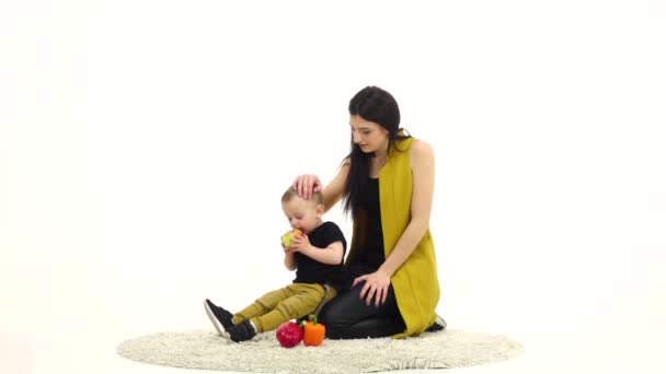 Bébé mange une pomme, à côté de sa mère. Fond blanc. Mouvement lent — Video