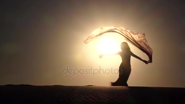 Dívka se závojem v jejích rukou tančí břišní tance na pláži. Silueta. Zpomalený pohyb — Stock video