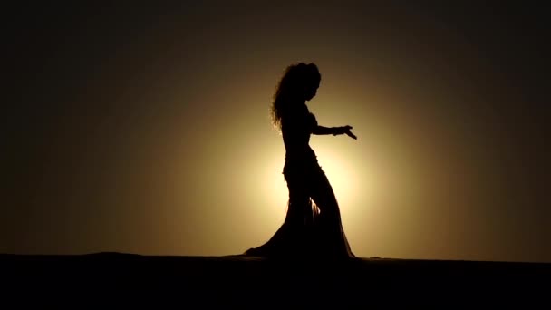 Menina executa bela dança do ventre no fundo do pôr do sol. Silhueta. Movimento lento — Vídeo de Stock