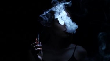 Karanlık bir odada kız elektronik sigara içiyor. Siyah arka plan. Siluet