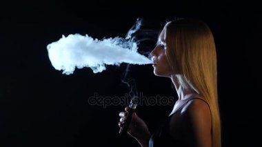 Sarışın geniş bir odada elektronik sigara içiyor. Siyah arka plan. Yan viwe