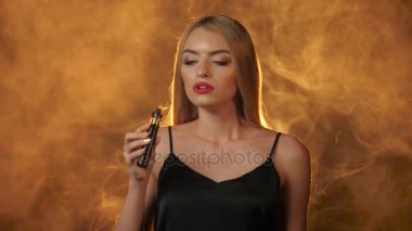 Kırmızı dudaklar ile sarışın sigara elektronik sigara ve gülümsüyor. Altın duman arka plan