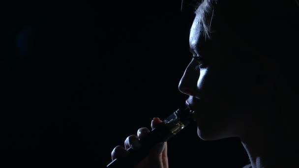 Девушка курит электронную сигарету. Чёрный фон. Закрывай. Силуэт — стоковое видео