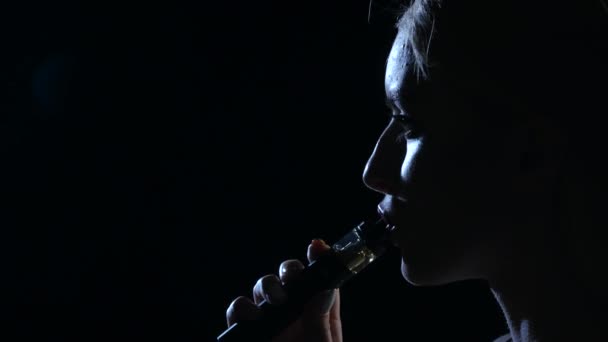 La ragazza fuma una sigaretta elettronica. Fondo nero. Chiudete. Silhouette — Video Stock