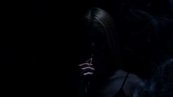 Una chica en un cuarto oscuro fuma un cigarrillo electrónico. Fondo negro. Silueta — Vídeos de Stock