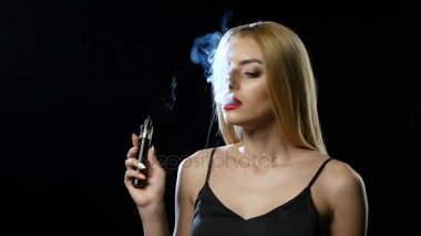 Sarışın geniş bir odada elektronik sigara içiyor. Siyah arka plan. Ağır çekim
