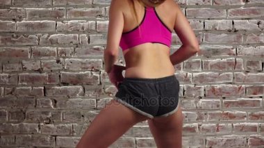 Esnek bir tuğla duvara şortlu kızla dans twerk. Ağır çekim. Yakın çekim