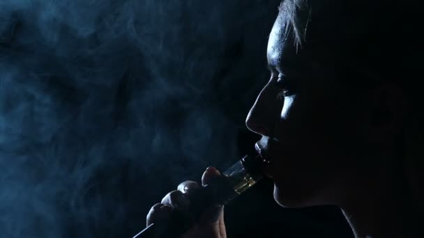 A rapariga fuma um cigarro electrónico. Fundo preto. Fecha. Silhueta. Movimento lento — Vídeo de Stock