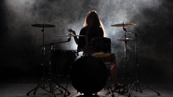 Una chica especialmente entrenada toca la batería. Fondo de humo negro. Silueta — Vídeos de Stock