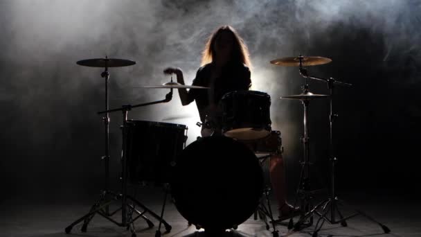 Girl es patadas de tocar la batería, tocando música enérgica. Fondo de humo negro. Silueta — Vídeos de Stock