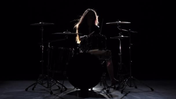 Girl es patadas de tocar la batería, tocando música enérgica. Fondo negro. Silueta. Movimiento lento — Vídeos de Stock