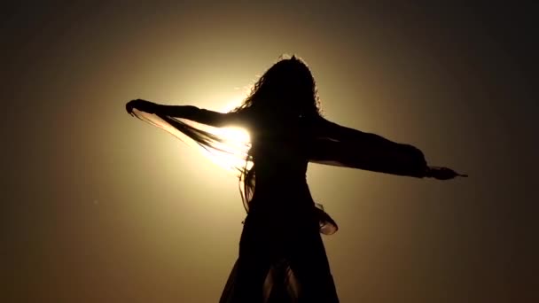 Meisje met een sluier in haar handen buikdans dansen op het strand. Silhouet. Slow motion — Stockvideo