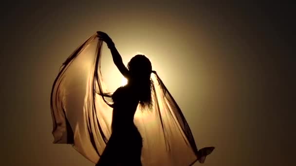 Девушка с вуалью в руках танцует танец живота на пляже. Силуэт. Медленное движение — стоковое видео