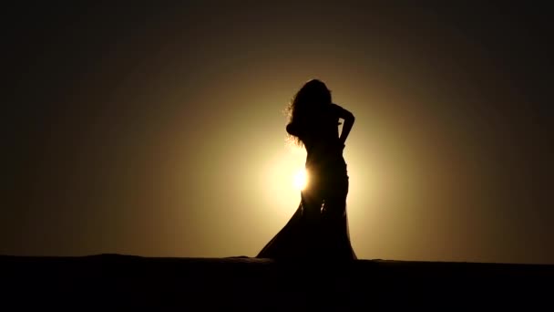 Chica está bailando danza del vientre contra la hermosa puesta de sol en la playa. Siluetas. Movimiento lento — Vídeo de stock