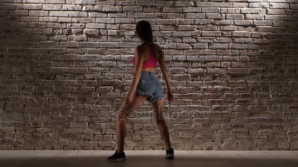 Woman in the crop top and denim shorts dance twerk against a brick wall — Stock Video