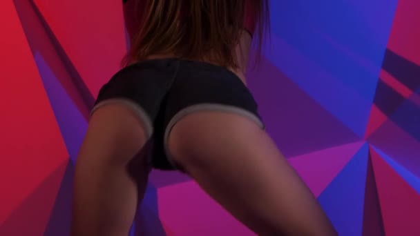 Mujer flexible moviendo su culo bailando twerk en pantalones cortos sobre fondo gráfico brillante. De cerca. — Vídeos de Stock