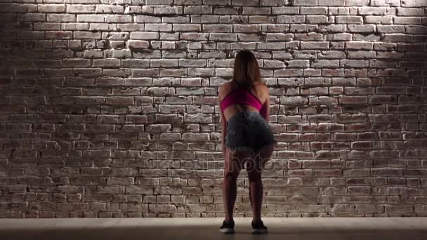 Fille sexy dans le haut de la récolte et shorts en denim danse twerk contre un mur de briques. Mouvement lent — Video