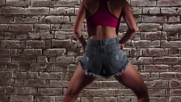 Femme élégante dans le crop top et short en denim danse twerk contre un mur de briques. Au ralenti. Gros plan — Video