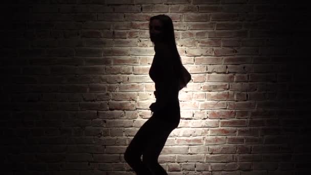 Danza twerk con ragazza in pantaloncini di jeans contro un muro di mattoni. Silhouette. Al rallentatore. Da vicino. — Video Stock