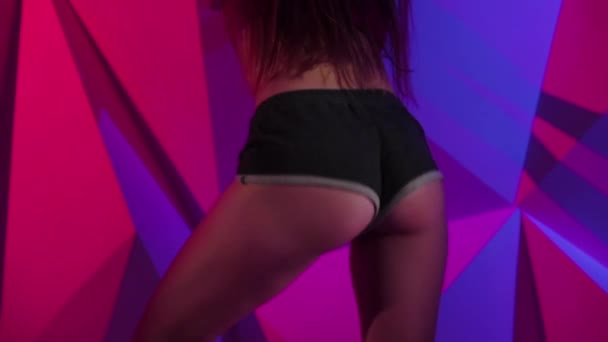 Mujer flexible moviendo su culo bailando twerk en pantalones cortos sobre fondo gráfico brillante. En cámara lenta. De cerca. — Vídeo de stock