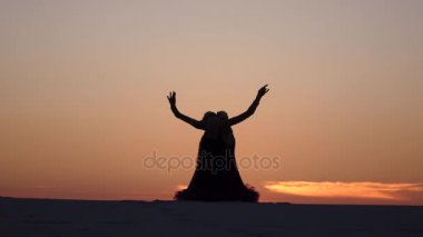 Dansçı cinsel arka planı ateşli bir günbatımı kum üzerinde dans ediyor. Siluetleri
