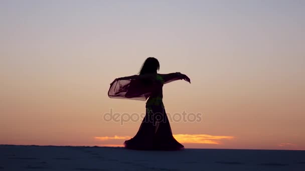 Danser seksueel danst op het zand tegen de achtergrond van een vurige zonsondergang. Silhouetten — Stockvideo