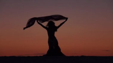 Kız incelikle eller bir günbatımı karşı bir örtü ile dans ediyor. Siluet