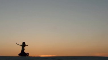 Kız oryantal güzel gün batımını karşı sahilde dans dans ediyor. Siluetleri